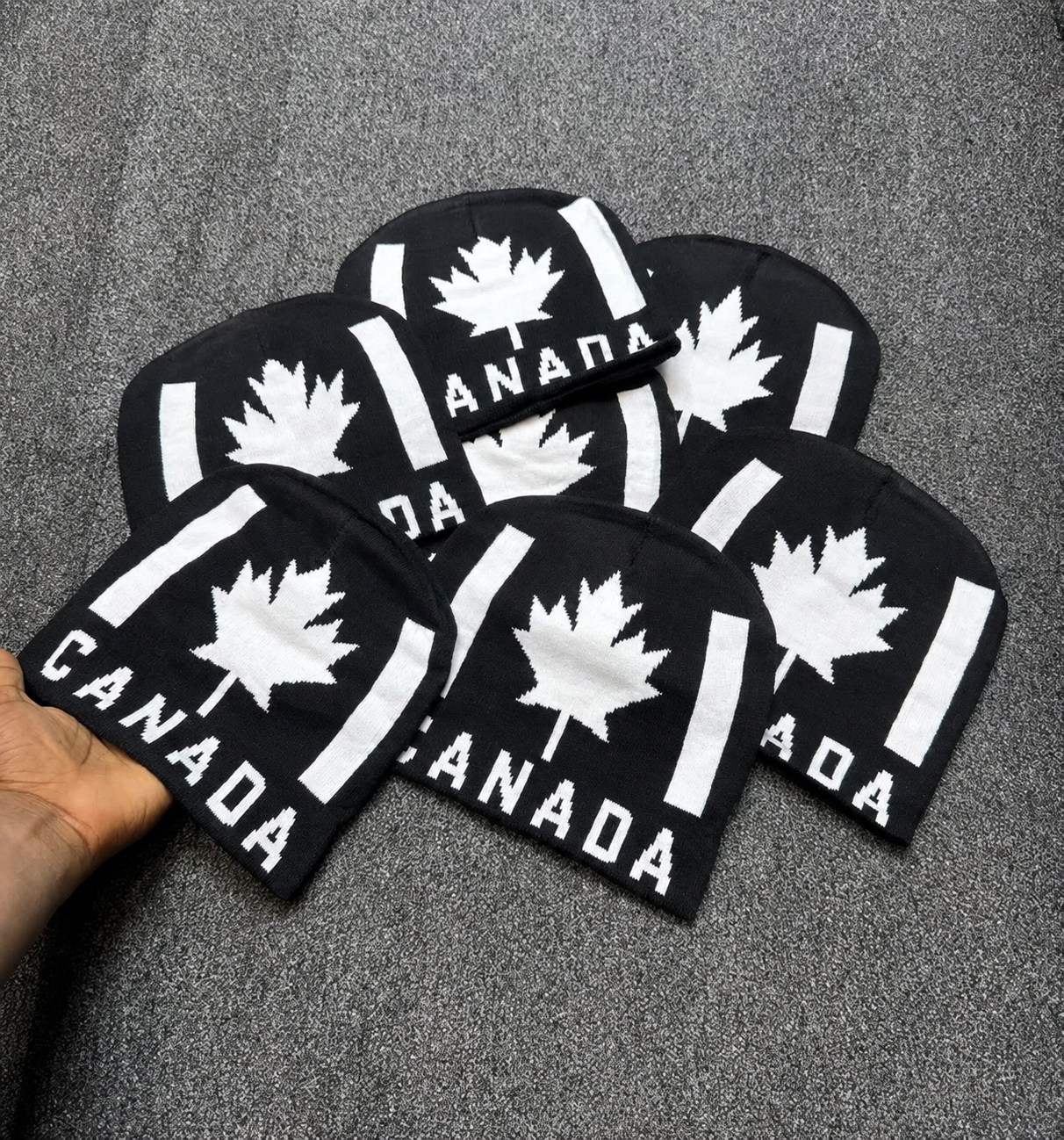 black knit beanie features a white pixelated maple leaf and "CANADA" text in a blocky font.