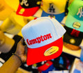 red flatbill snapback hat features prominent red "Compton" embroidery in an Old English font.