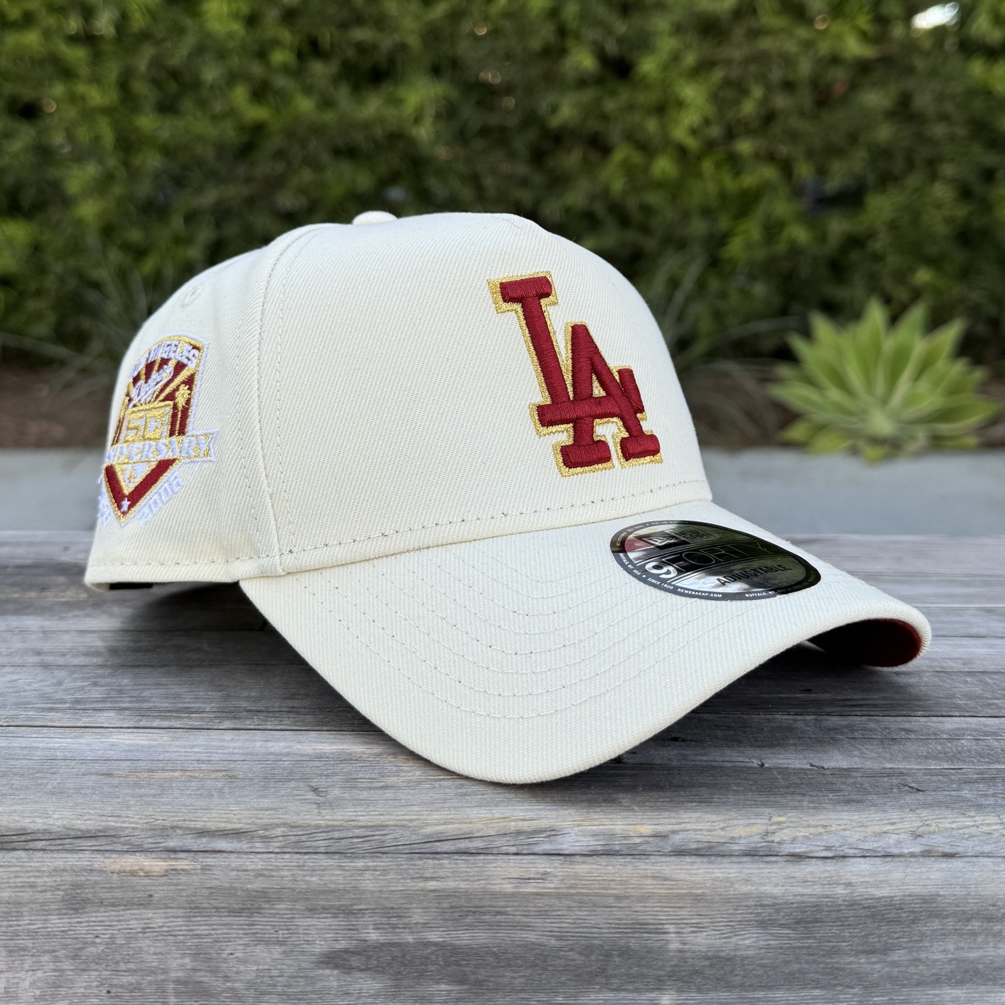cream New Era 9FORTY A-Frame snapback features a red "LA" logo with gold outlining and a 50th Anniversary side patch